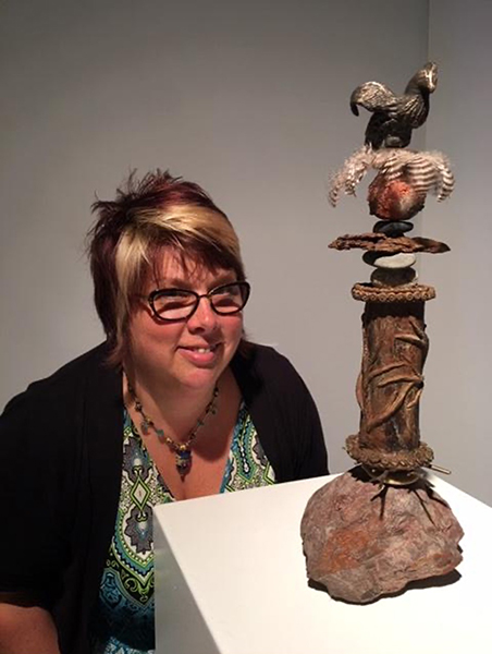 Art educator and artist Alice Bordenkircher Tavani with her work In the Beginning (2016), a mixed-media, vertical work with rock-form, feather, and animal figure.