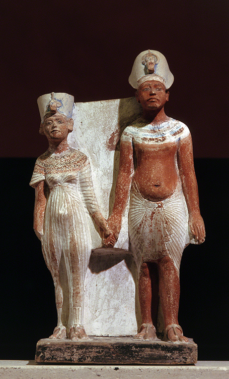 Statuette of Akhenaten and Nefertiti, found at Amarna (1345–1337 BCE). Ancient Egyptian pharaoh and queen hold hands and stand against a white background.