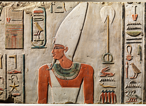 Painted limestone relief of Nebhepetre Mentuhotep II with figure in front/profile pose with tall white headdress, white clothes, and green collar with hieroglyphics.