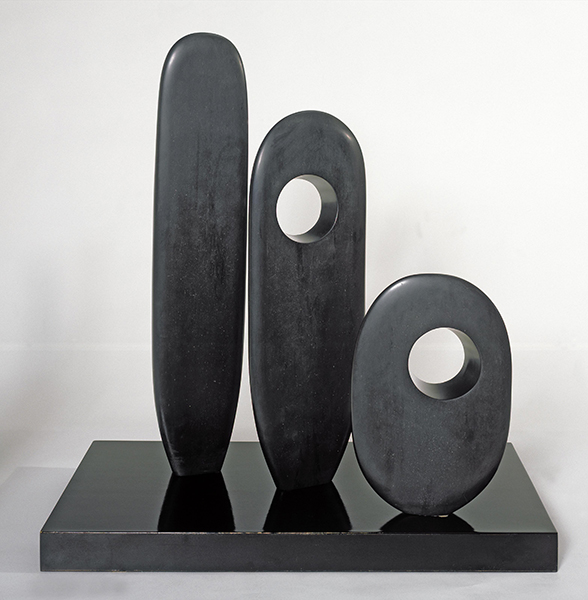 Slate sculpture by Barbara Hepworth titled Three Standing Forms. Three dark gray vertical oval forms that get smaller from left to right. The two forms to the right have holes creating negative space.