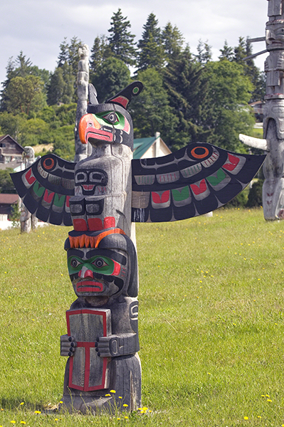 Cedar totem by Bruce Alfred titled Thunderbird and Copper Totem (1995). Figure holding a copper (tlakwa) at the base and a thunderbird above.