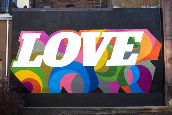 Mural by Cey Adams titled Love (2018). Wall with the word LOVE in white with colorful swirls behind the letters against a black background.