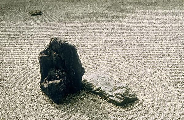 Rock with raked sand around it in a dry garden of a Zen temple.