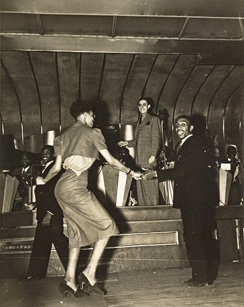 Photograph by Lucy Ashjian titled Savoy Dancers (ca. 1937). Black-and-white photograph of a man and a woman dance in front of a live band.