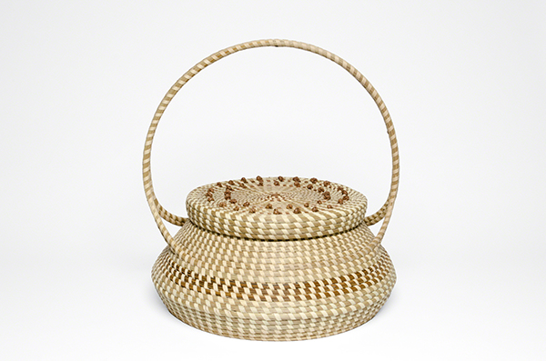 Coiled box by Mary A. Jackson (2012). Covered box with a slender, elegant handle made from alternating rows of sweetgrass and bulrush, with pine needle French knots.
