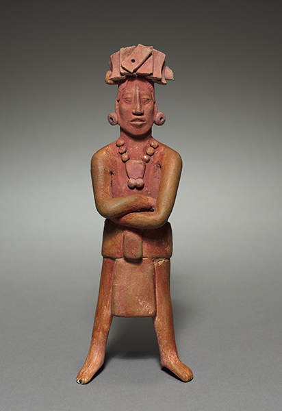 Terracotta male figure (317-987 CE) from Jaina Island, Maya Culture, Mexico. Male figure wearing a headdress, earspools, necklace, and skirt stands with arms folded and legs apart.