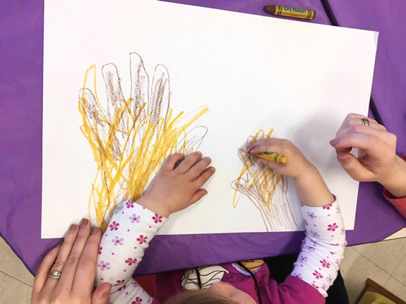 Haley and Lisa color the tree trunks and branches formed from their hands and arms.