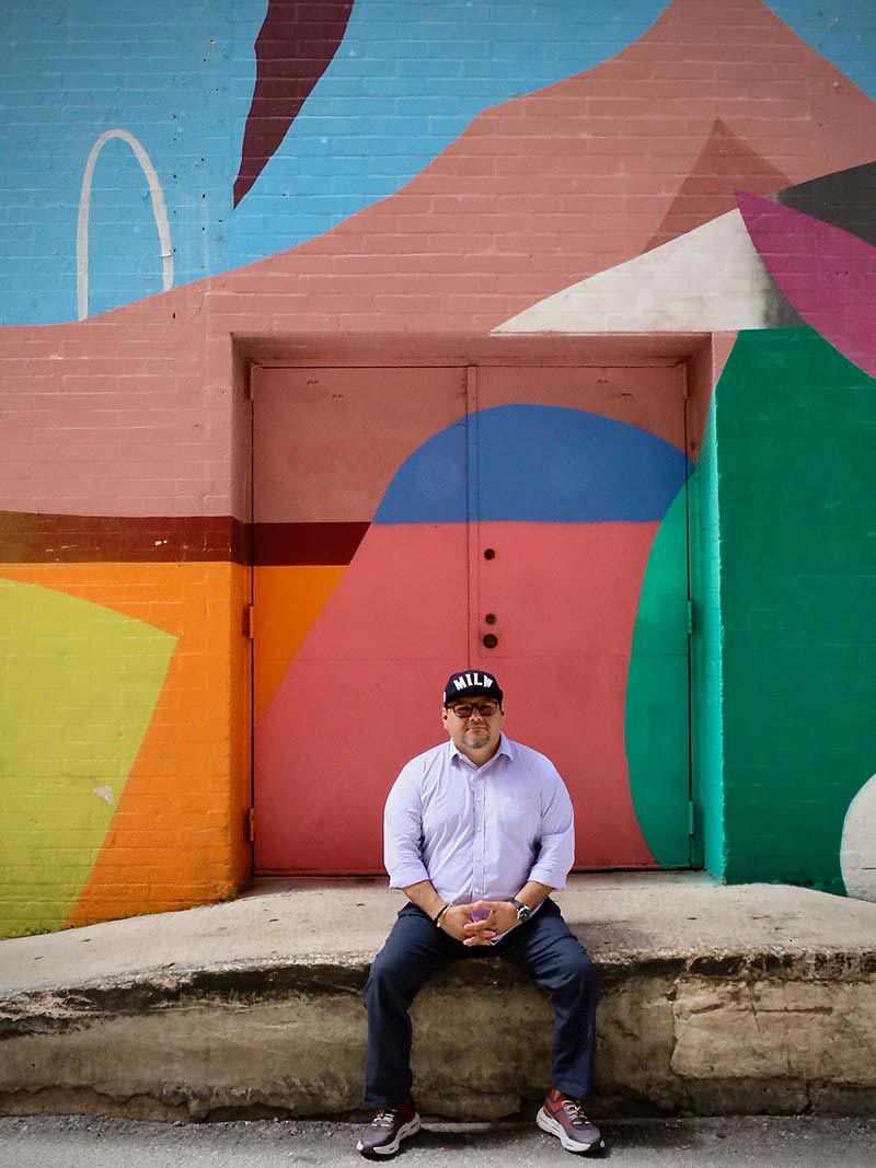 Frank Juárez sitting in front of a mural in downtown San Antonio. Photo by Mary Lou Mayr.