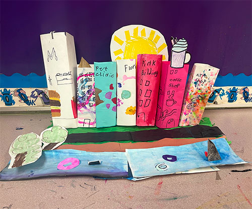 A paper model of the Chicago skyline from the article Unwanted Artwork Olympics in which elementary students participate in an art challenge utilizing discarded works to create something new