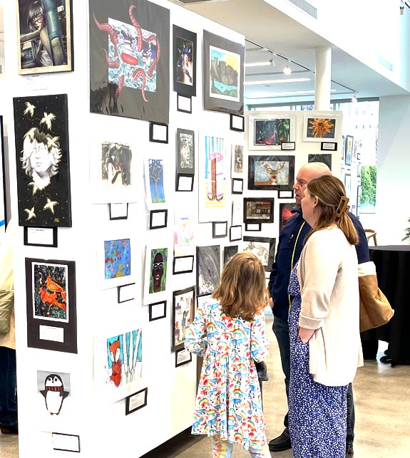 Visitors admire student artwork on view.